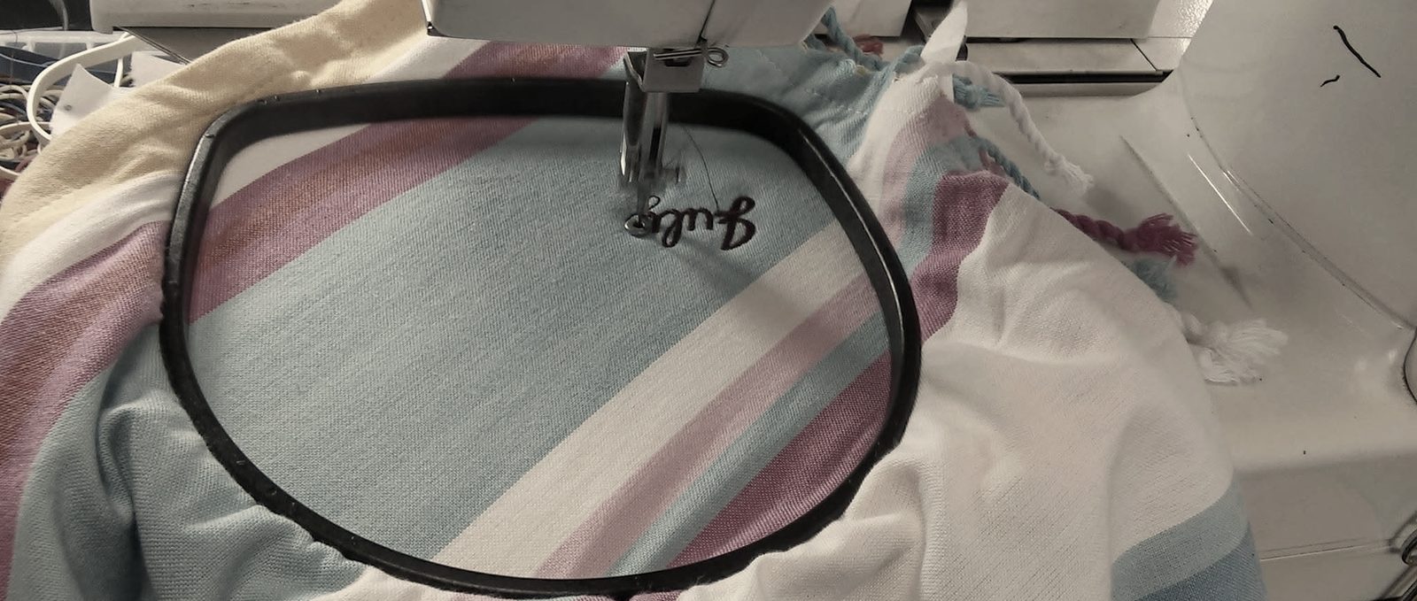 A striped beach towel hooped on an embroidery machine with a small script name stitched