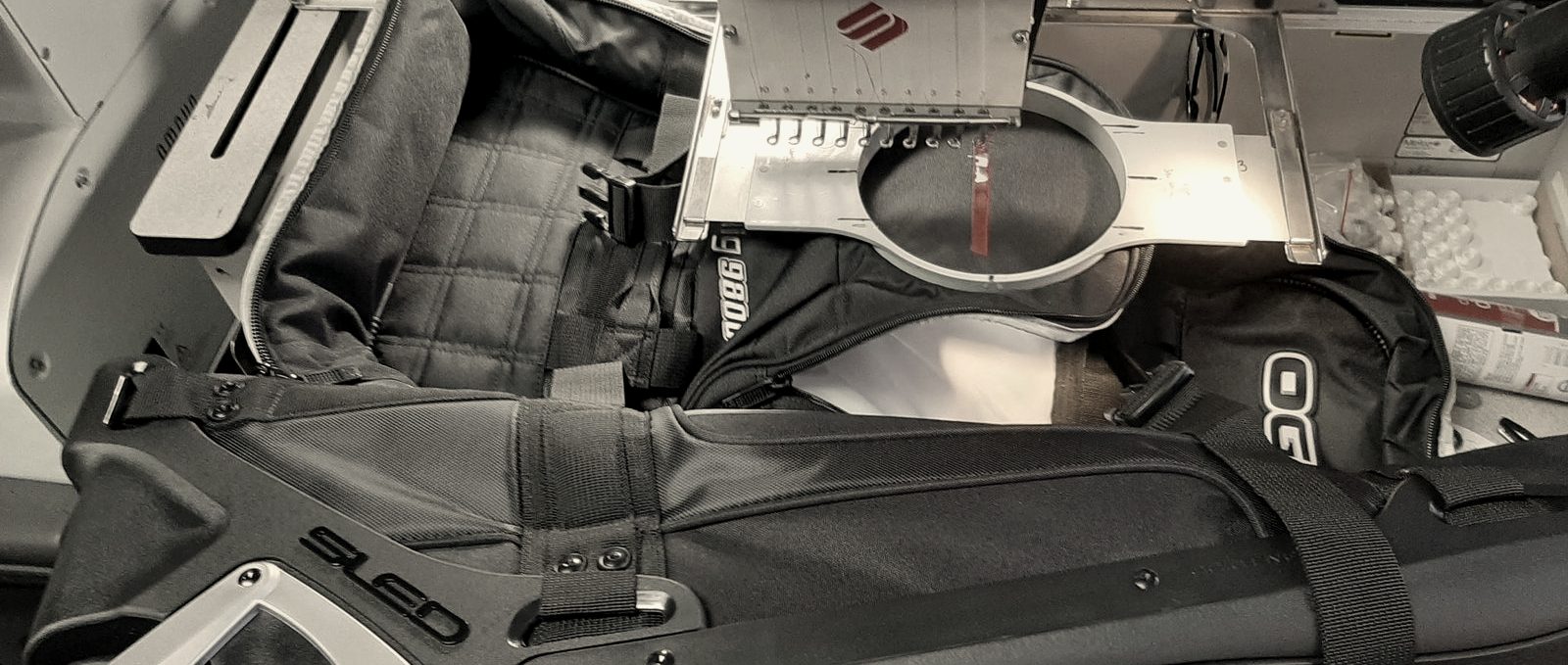 A black travel bag hooped on an embroidery machine at MMM Embroidery