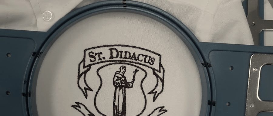 A school crest stitched in maroon on a white shirt, still in the blue hoop