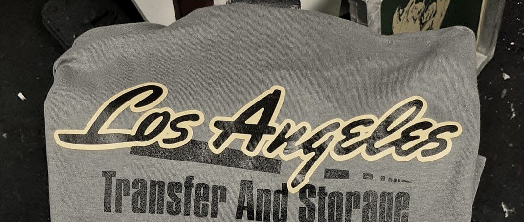 A stack of heather grey tees printed with a moving company's name in yellow and white