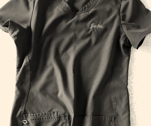 A charcoal scrub top with a first name embroidered in pink script