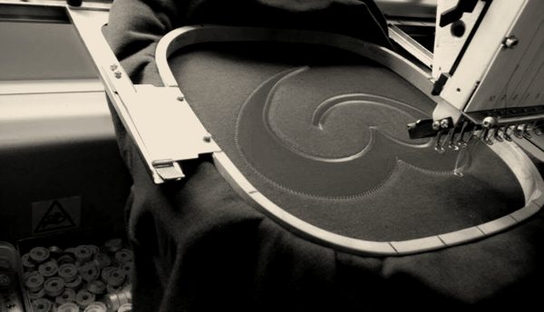 A red swirl logo being stitched on a navy jacket in the hoop