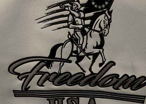 An embroidered patriotic design: a rider with a flag over script lettering