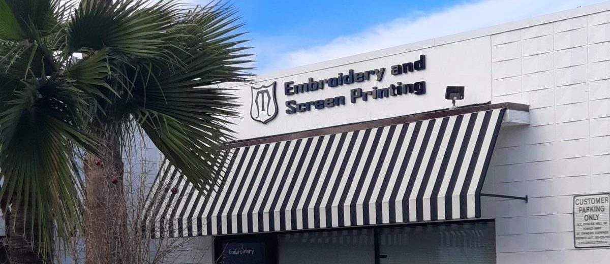 The MMM Embroidery storefront in Newhall Square: the shield sign and striped awning