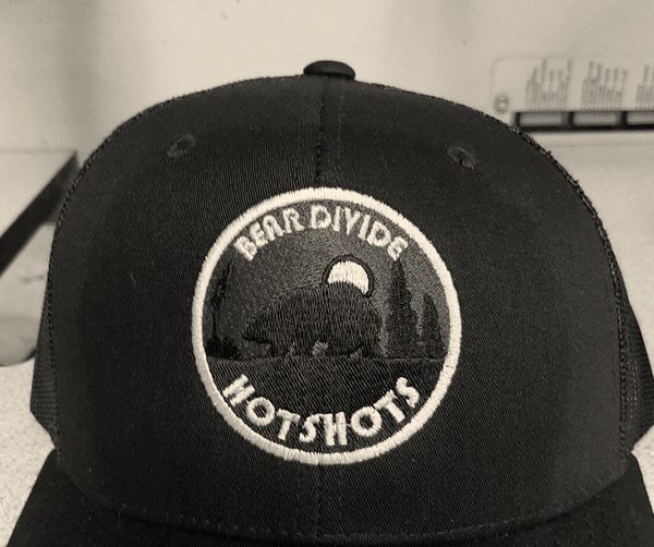 An embroidered patch-style logo on a wildland fire crew cap