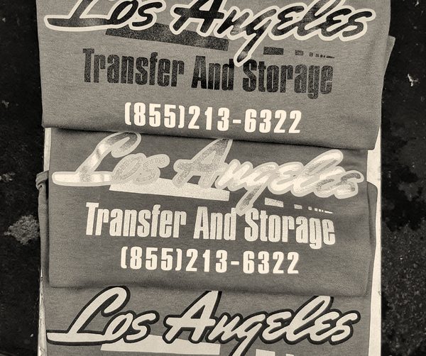 Crew tees printed with a moving company's name, stacked in the shop