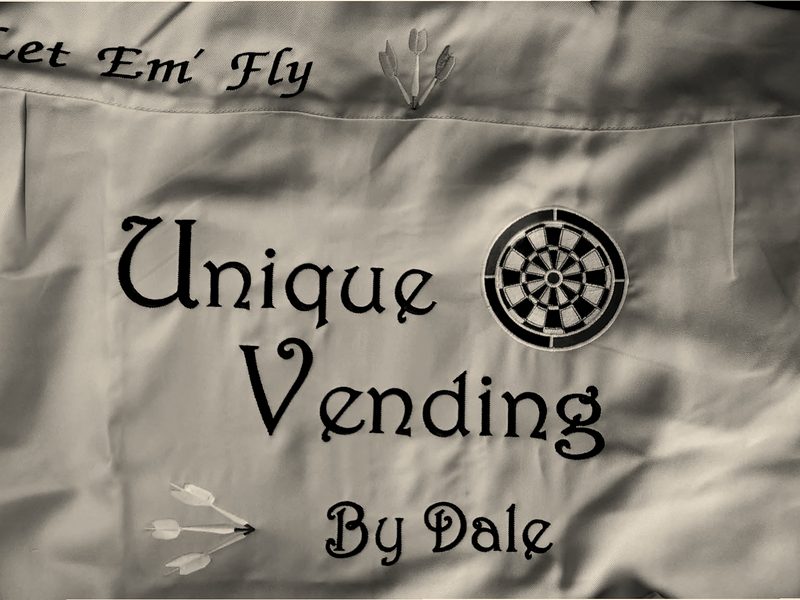 A khaki apron embroidered with a business name in script and a dartboard logo