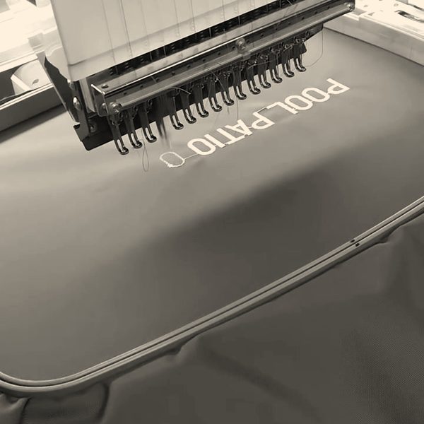 A Barudan head stitching a business name in white on dark green fabric