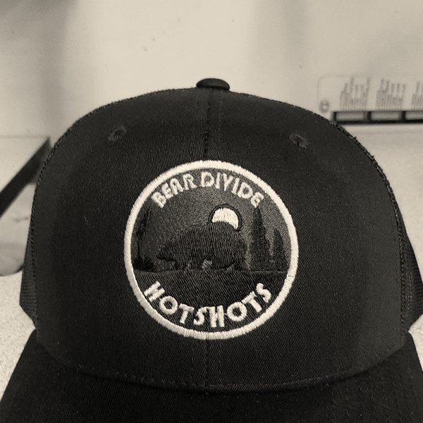 A black trucker cap with a round embroidered fire crew patch on the front