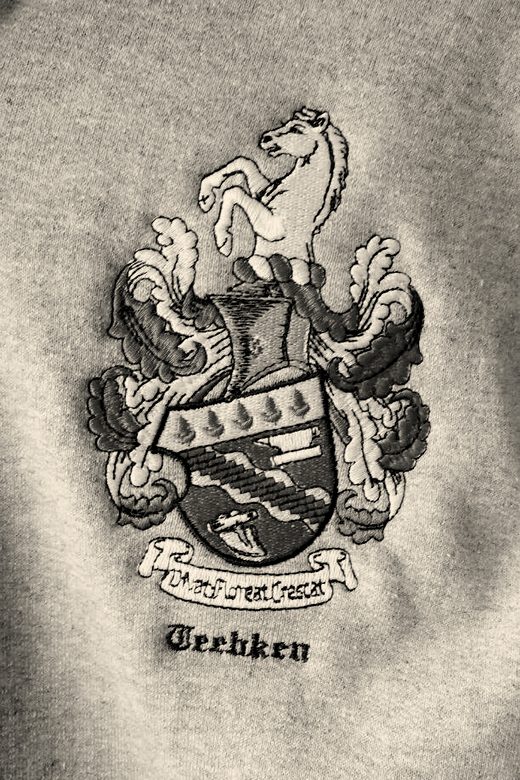 A detailed family crest with a white horse and green mantling embroidered on grey fleece