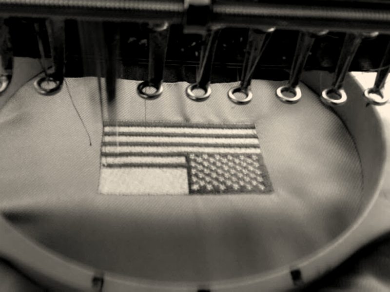 A US flag stitched on olive fabric in a round hoop, needles above