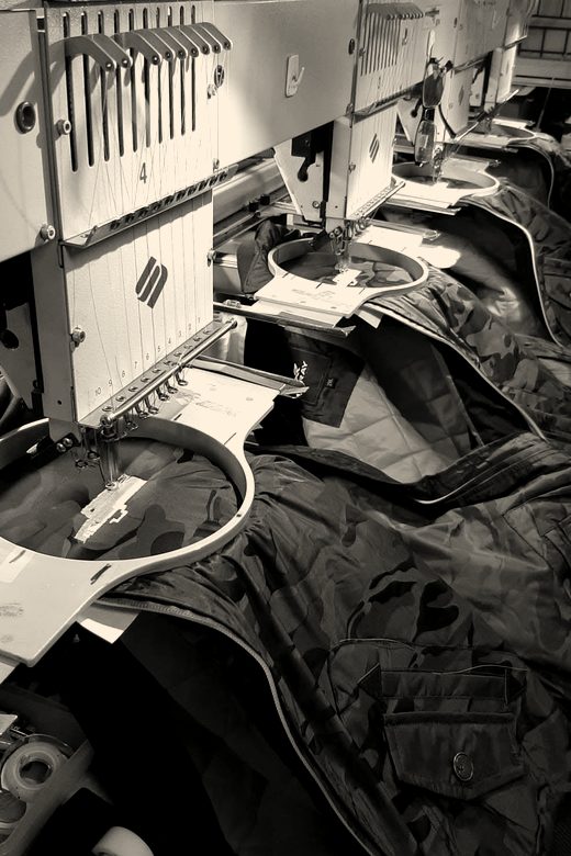 Navy jackets with orange lining hooped across a multi-head embroidery machine