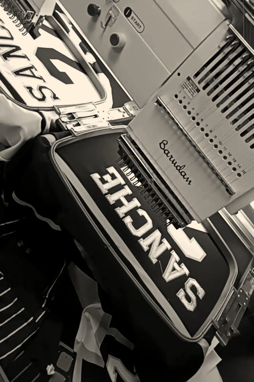 Two Barudan heads stitching a surname plate on pinstripe baseball jerseys