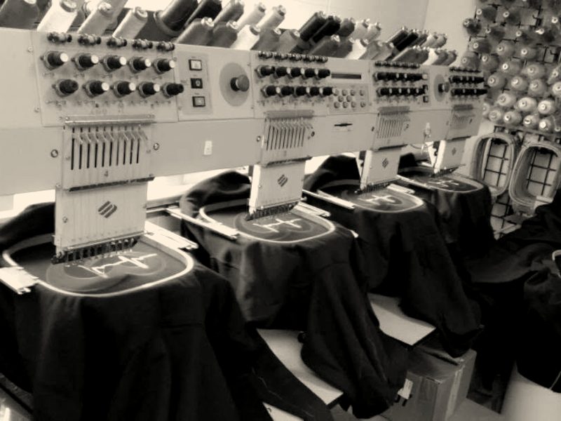 Navy jackets hooped across a multi-head machine, a red logo stitching on each one, thread wall behind