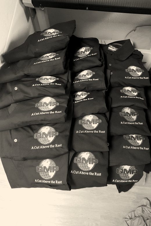 Two stacks of folded black polos with a company logo on the chest