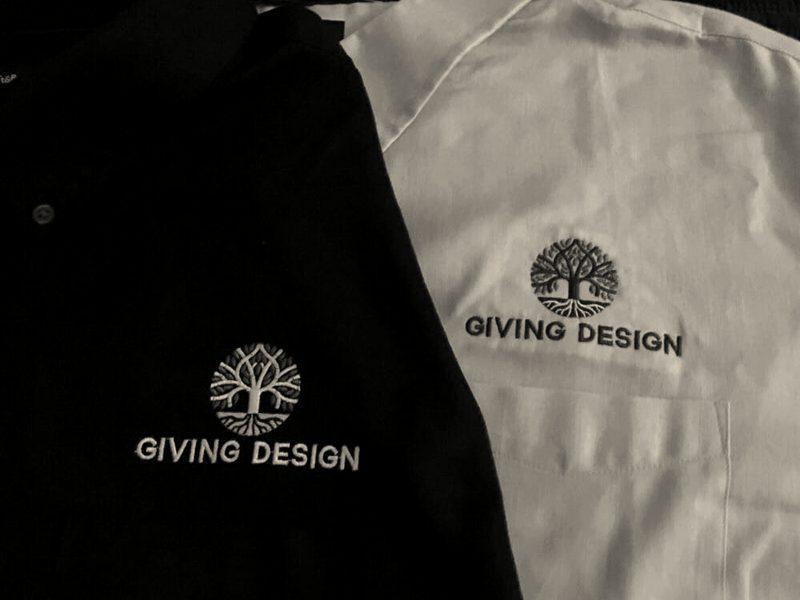 A black polo and a white polo with the same tree logo embroidered on the chest