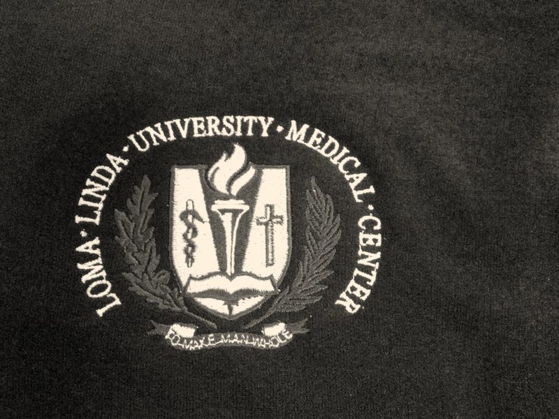 A medical center's crest embroidered in red, gold and white on the left chest of a navy zip jacket