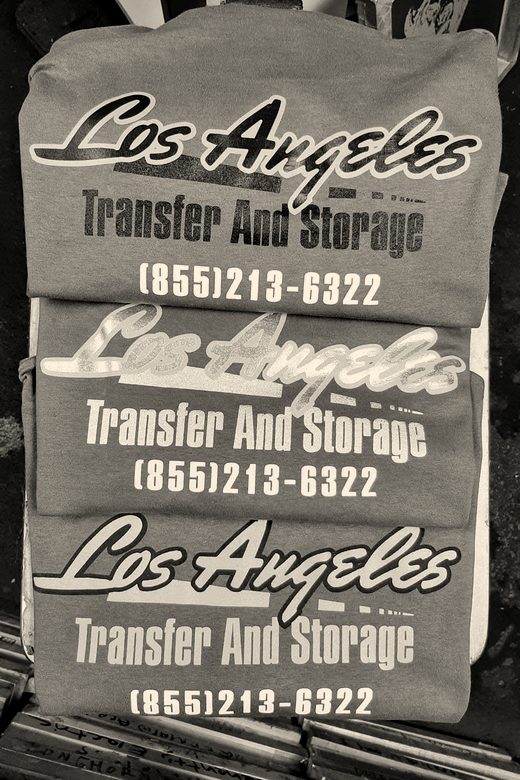 A stack of heather grey tees printed with a moving company's name in yellow and white