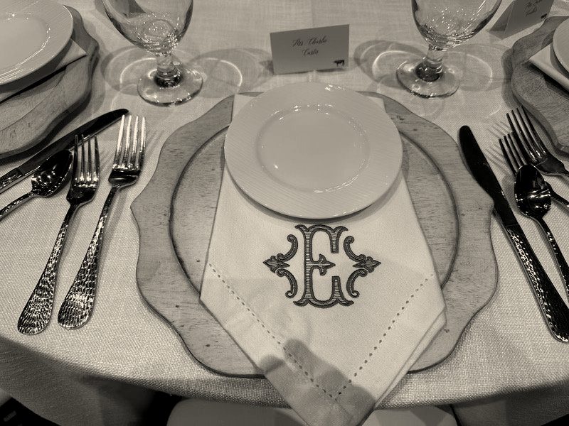 A white napkin with a large sage green monogram letter on a set wedding table