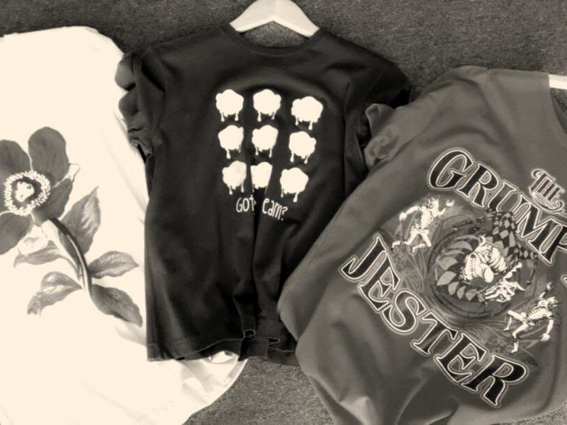 Three printed tees on hangers: a pink flower, a navy tee with pastel icons and a red tee with a jester