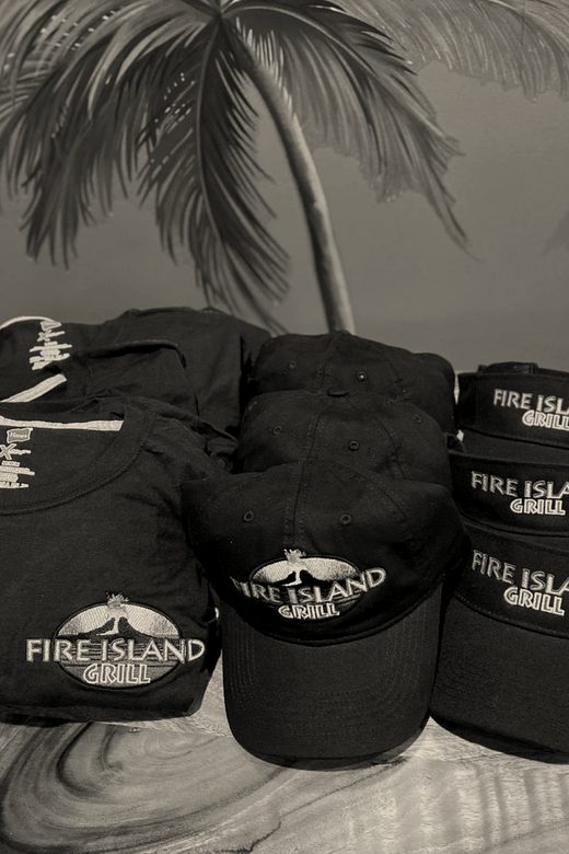 A stack of navy caps and folded navy tees with a restaurant's logo, on a wood counter