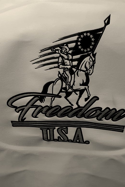 An embroidered design of a rider carrying a flag over script lettering, on white fabric