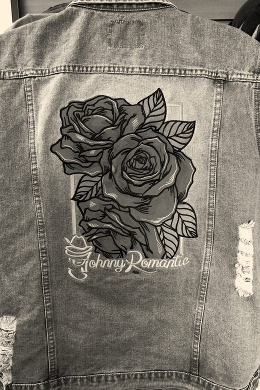 A large embroidered bouquet of red roses with green leaves across the back of a denim vest