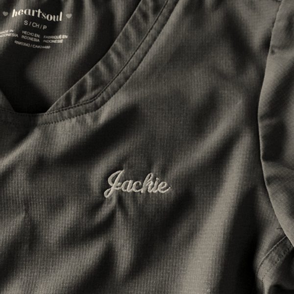 A first name in pink script embroidered on a charcoal scrub top