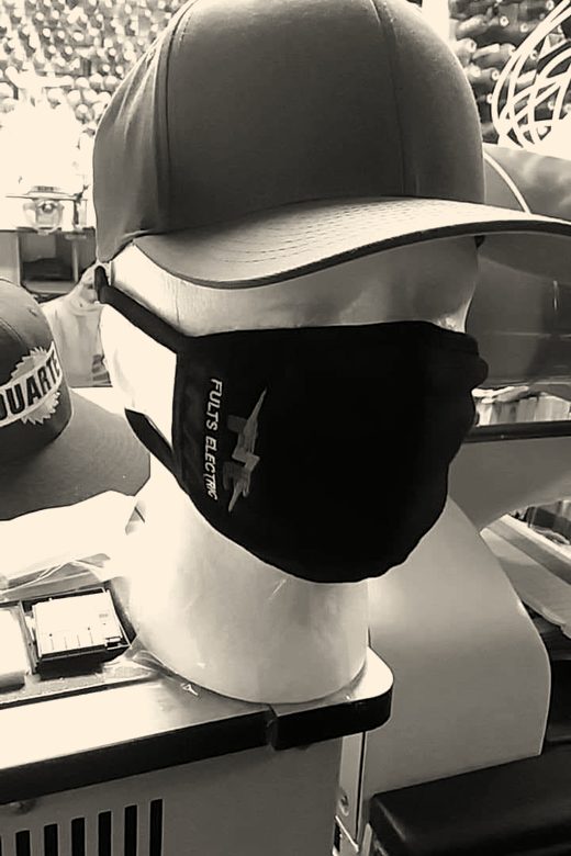 A black face mask embroidered with an electrical contractor's logo, on a mannequin head under an olive cap