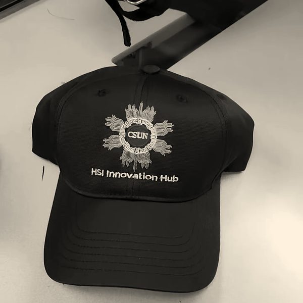A finished black cap with a gold and red sun emblem and a program name